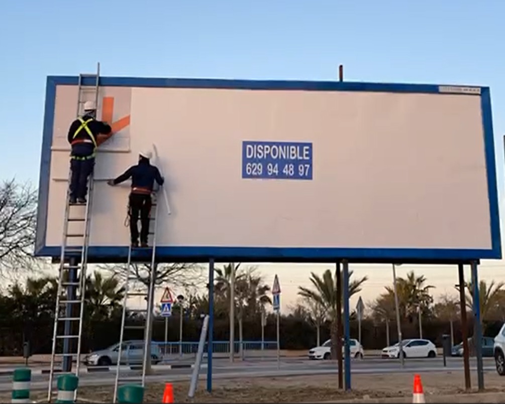 Operarios trabajando en una valla publicitaria de Vallas Donde Vayas, con marco y cuatro postes azules.